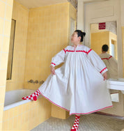 Person wearing a white dress with red trim in a bathroom with yellow tiles and a chandelier.